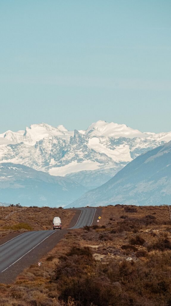 pexels-photo-17613106-17613106 Vehicle on a highway leading to majestic snowy mountains under a clear blue sky.